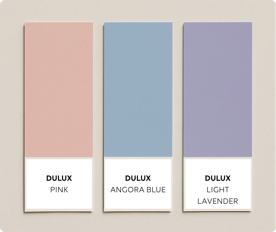 Three pastel Dulux swatches are arranged vertically against a soft off-white backdrop. From left to right: Pink Rafflie (soft pink), Powder Blue (light blue), and Lavender (soft purple), each labeled with Dulux branding.